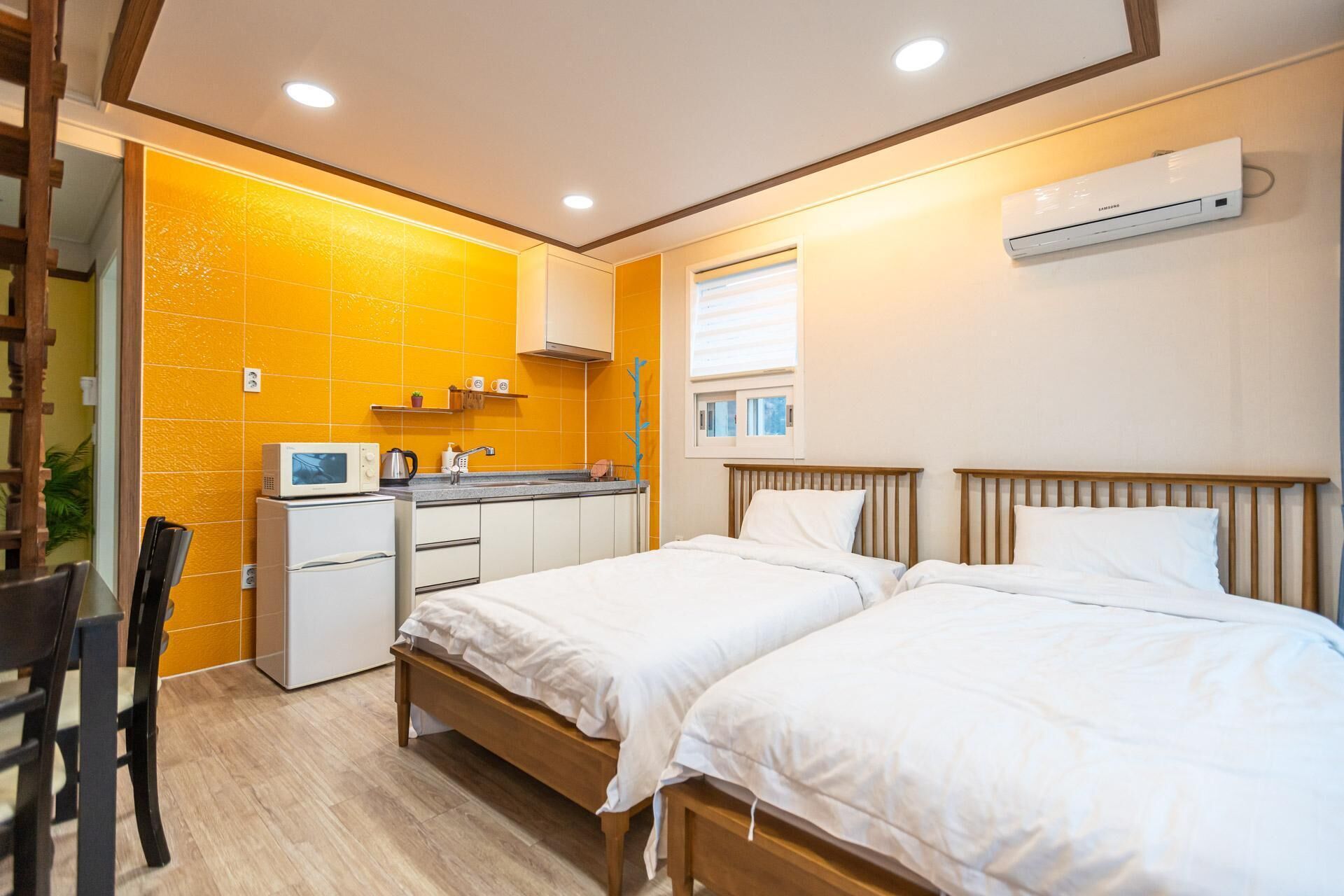 A compact hotel room with two beds, a kitchenette, and a window.