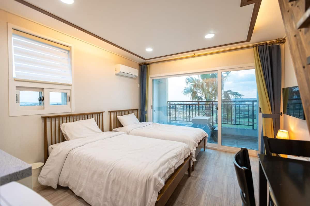 A hotel room with two beds, a desk, and a balcony with a view.