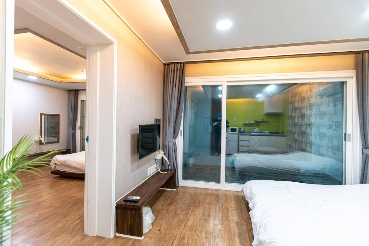 A hotel room with a bed, a desk with a computer, a TV, and a sliding glass door to the kitchen.