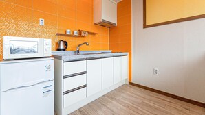 Une cuisine compacte avec des meubles blancs, un four à micro-ondes, une bouilloire et un évier.