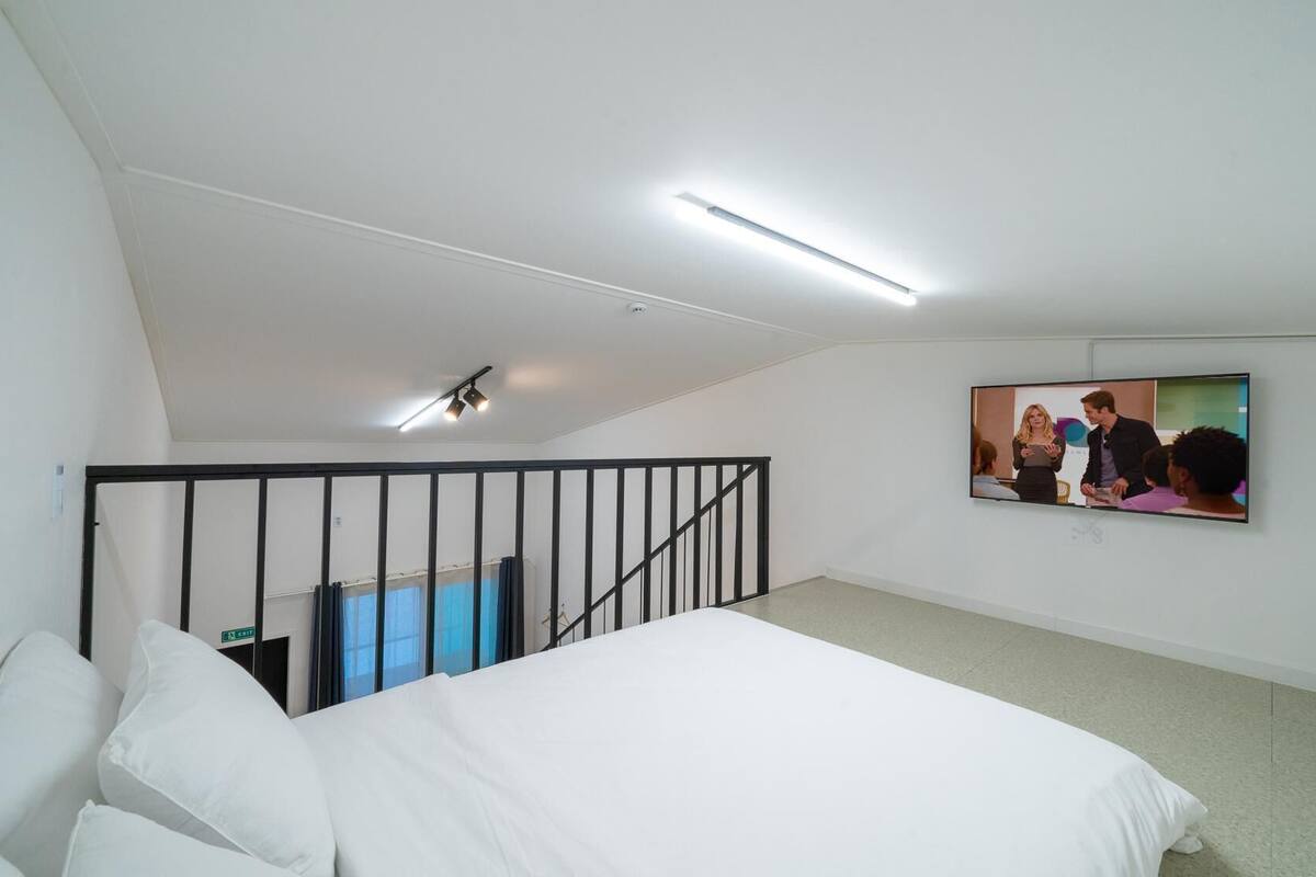 A bedroom with a bed, a TV mounted on the wall, and a staircase.