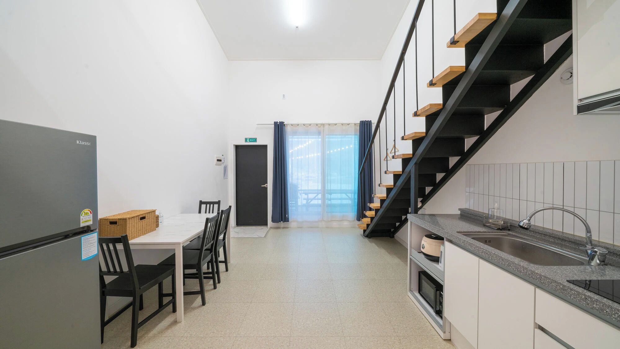 A modern kitchen with a built-in refrigerator, a dining area with a table and chairs, and a staircase with wooden steps.