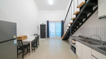 A modern kitchen with a built-in refrigerator, a dining area with a table and chairs, and a staircase with wooden steps.