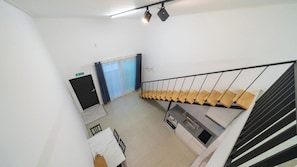 Una escalera con barandilla de madera y pasamanos de metal negro, que lleva a una plataforma con una zona de cocina que incluye un fregadero y una estufa.
