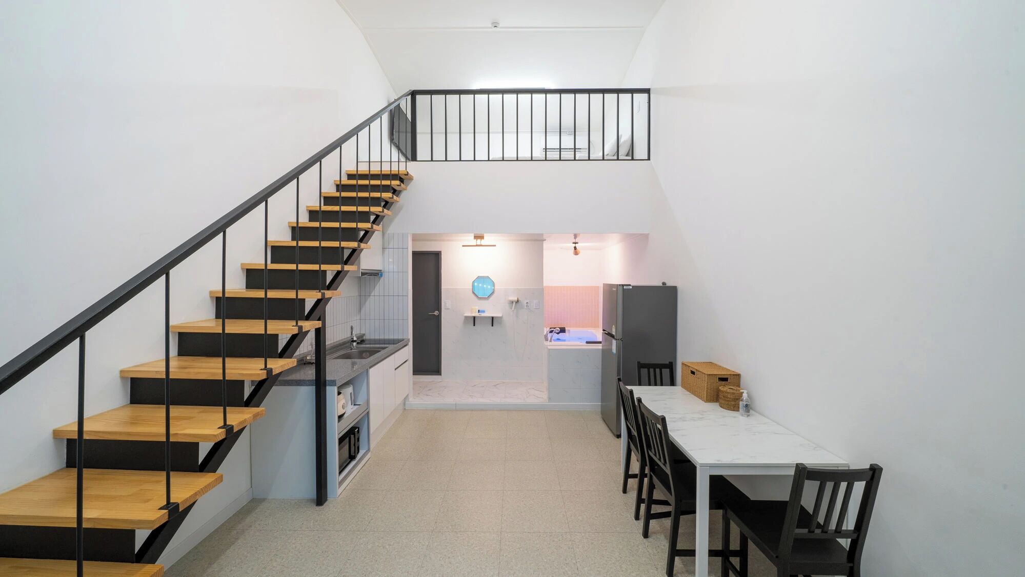 A modern interior with a staircase, kitchen, dining area, and a small bathroom.