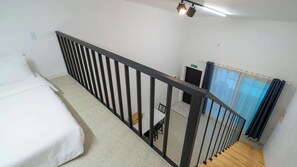 Ein Zimmer mit einem Bett, einer Treppe mit Geländer, einem Tisch mit Stühlen und einem Fenster mit Vorhängen.