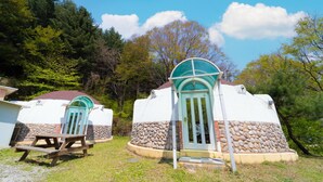 Two yurts with stone bases and turquoise roofs, surrounded by trees. - Yangpyeong Santa Pension (Yangpyeong)