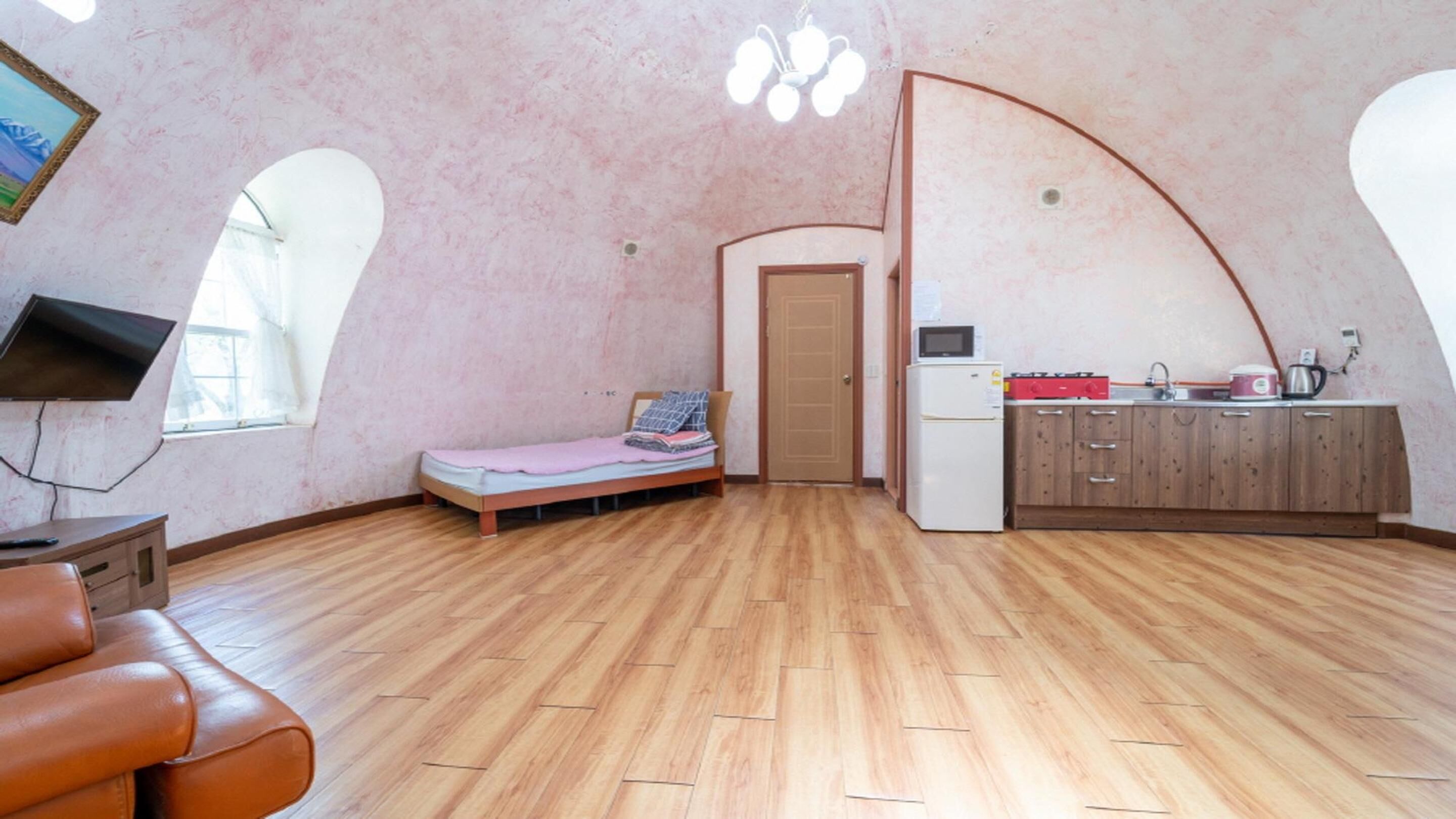 Una habitación compacta con cama, kitchenette, televisor y piso de madera.