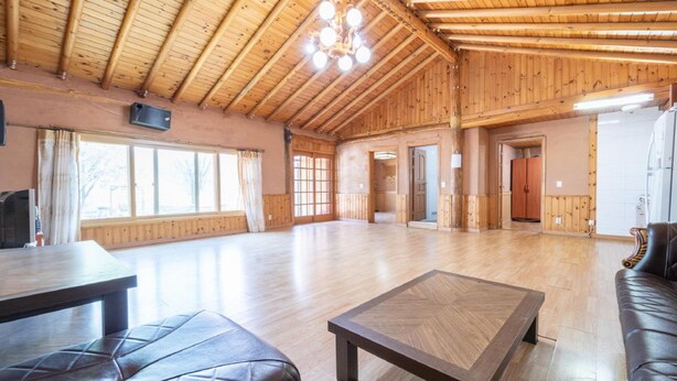 A spacious room with wooden walls and ceiling, a large window, a table, and a sofa. - Yangpyeong Santa Pension (Yangpyeong)