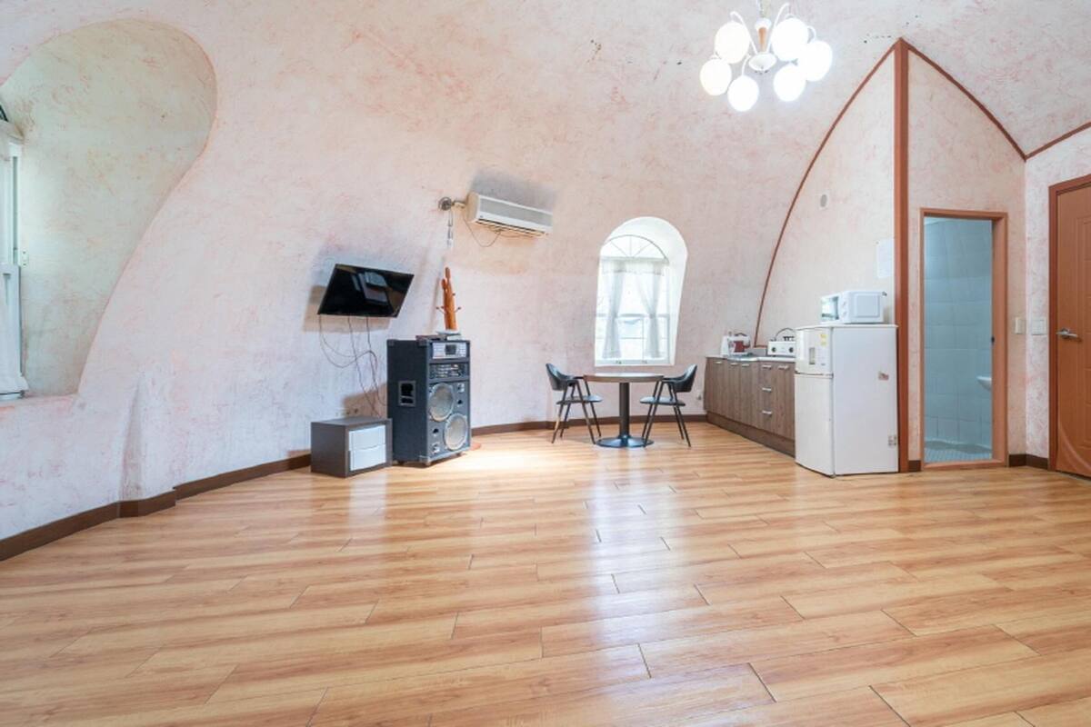 A spacious room with a wooden floor, a dining area with a table and chairs, a kitchen area with a refrigerator and microwave, and a large arched doorway.