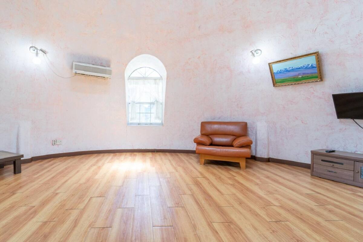 A spacious room with a wooden floor, a leather armchair, a bench, a small cabinet, and a painting on the wall.