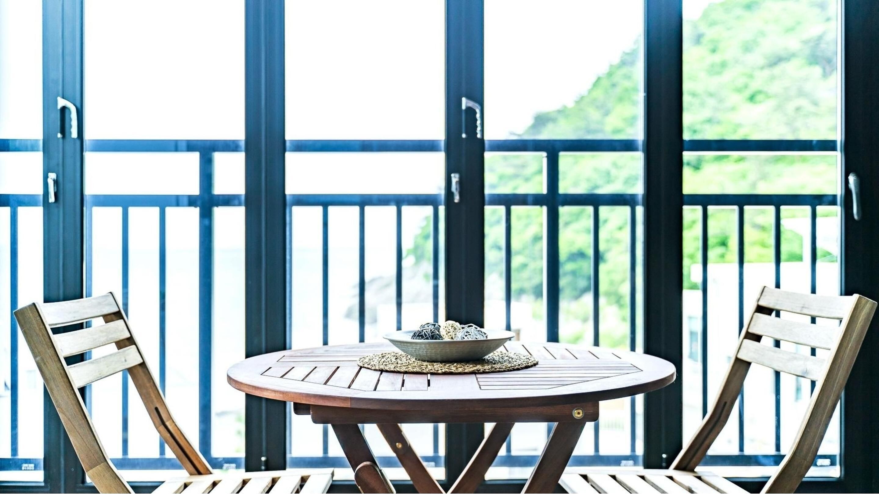 Ein Holztisch mit einer Schale Snacks auf einem Balkon mit blauen Geländern und zwei Holzstühlen.
