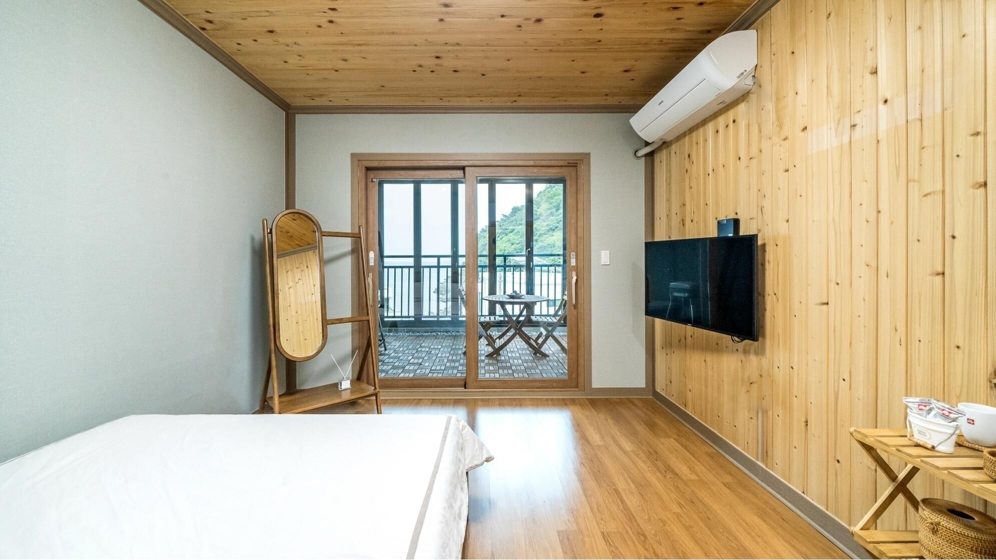 A room with a bed, a television mounted on a wooden wall, and a sliding glass door leading to an outdoor area with a table and chairs.