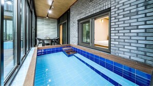 A modern indoor pool with blue tiles, a brick wall, and a window with a bed visible through it. - Namhae Yanghwa Seaside Pension (Namhae)