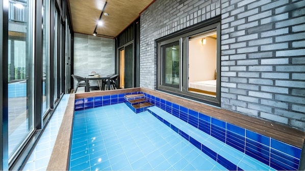 Een modern binnenzwembad met blauwe tegels, een bakstenen muur en een raam waardoor een bed zichtbaar is.