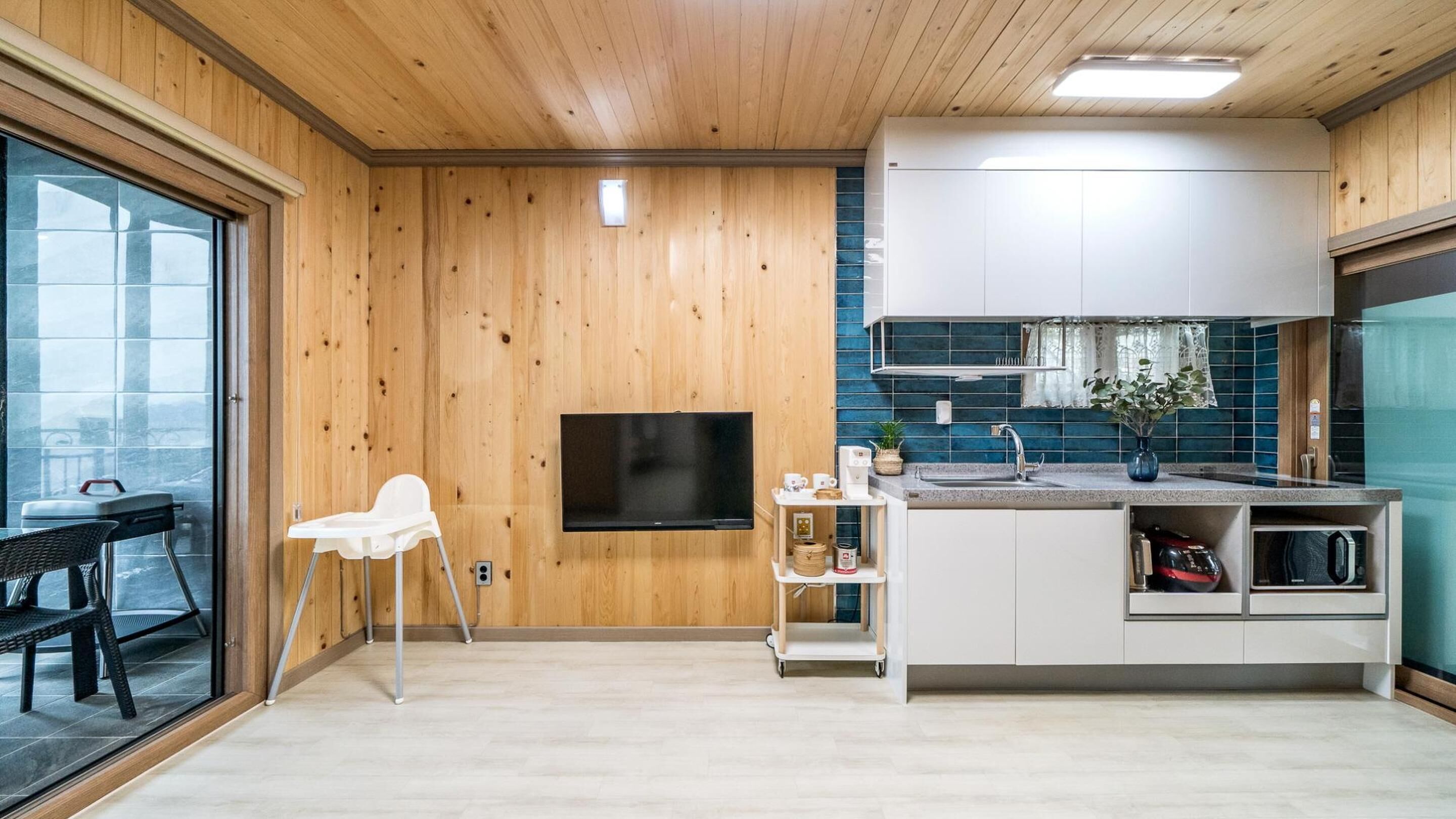 A modern kitchen with wooden walls, a flat-screen TV, and a dining area with a chair and table.