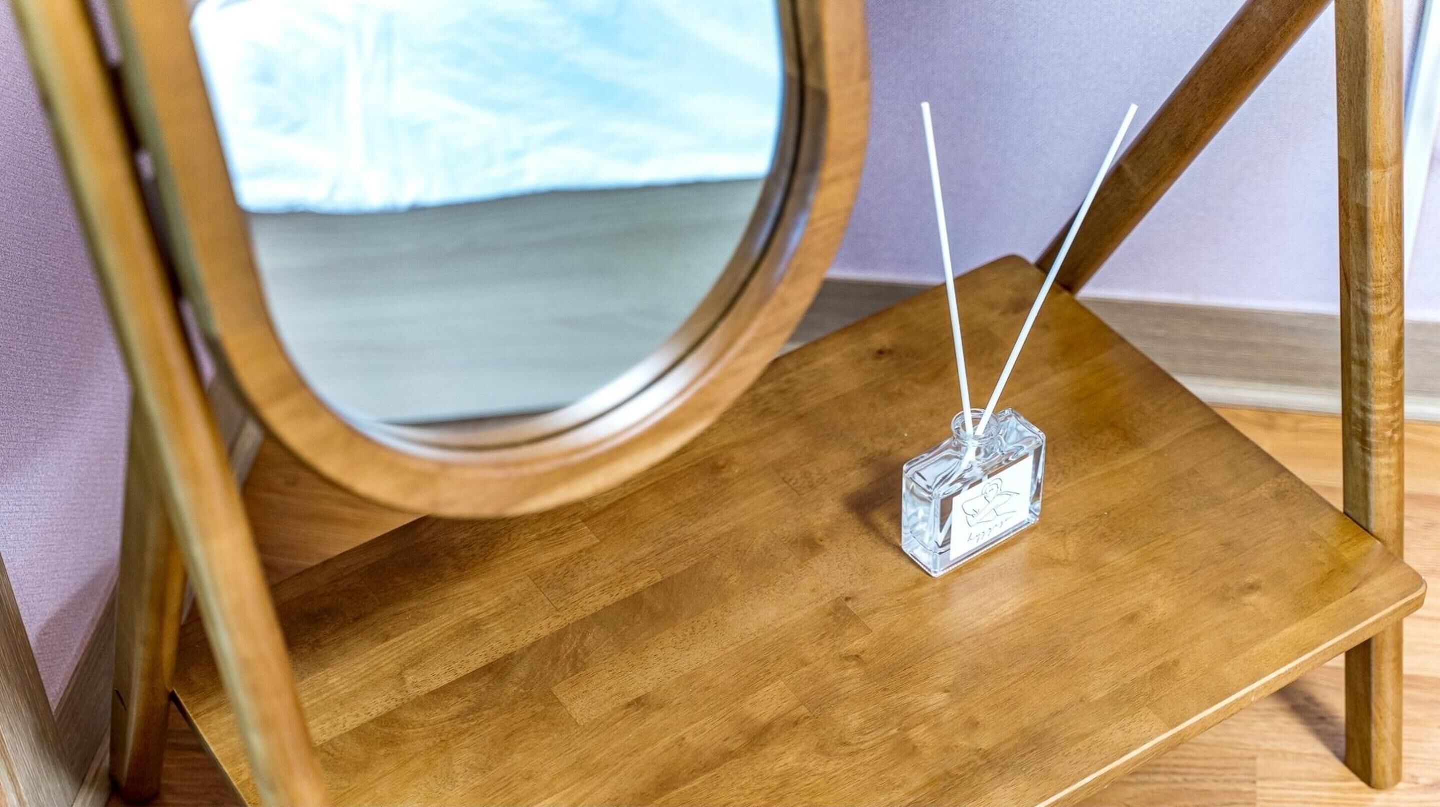 Ein Holzstuhl mit einem runden Spiegel und einer kleinen Glasflasche mit zwei weißen Stöcken.