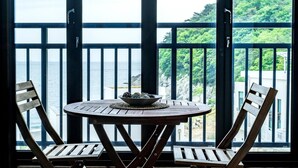 A round wooden table with a bowl of snacks, two wooden chairs, and a view of the sea through a balcony railing. - Namhae Yanghwa Seaside Pension (Namhae)