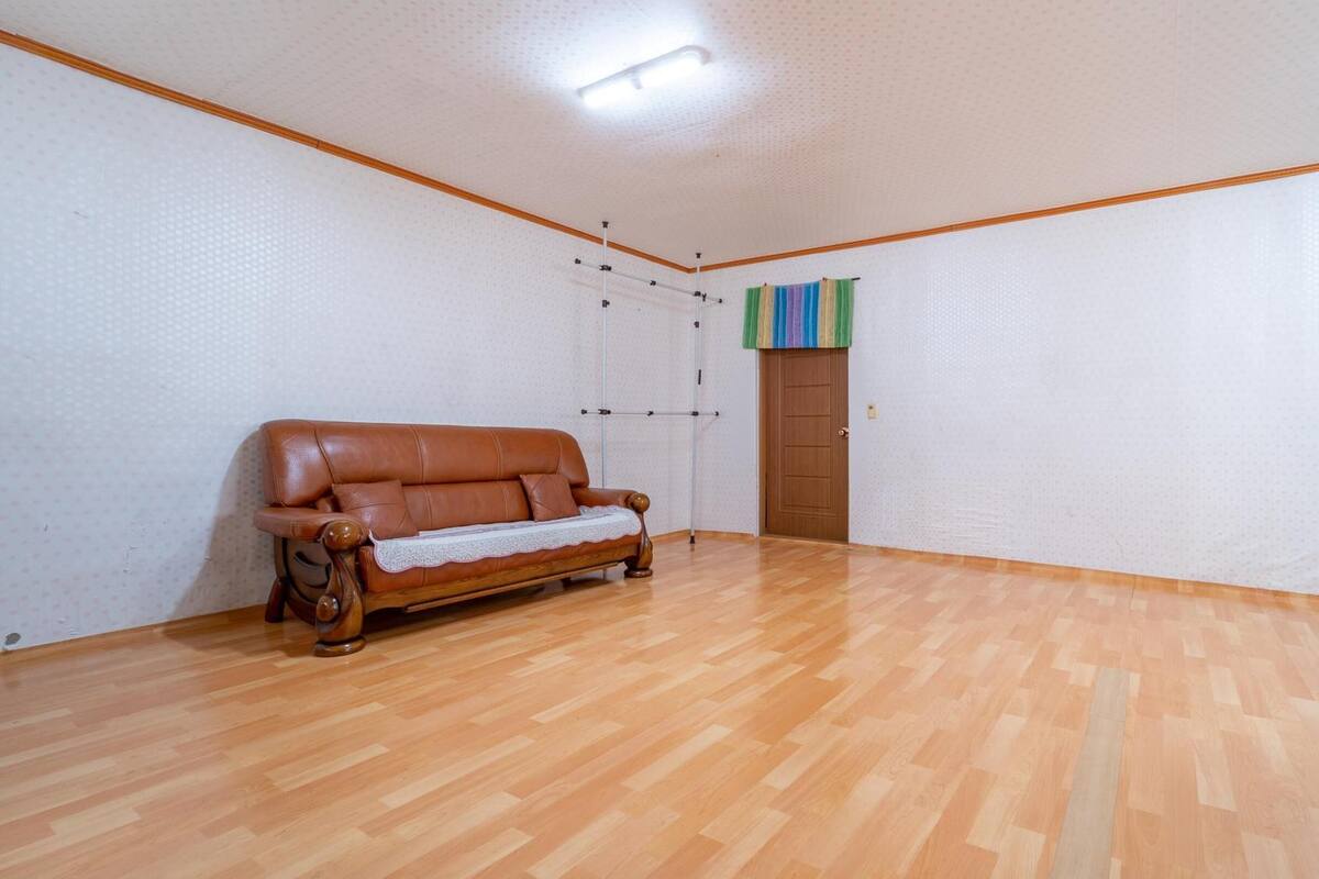 Ein geräumiger Raum mit Holzboden, einem braunen Ledersofa und einer Tür mit bunter Vorhang.