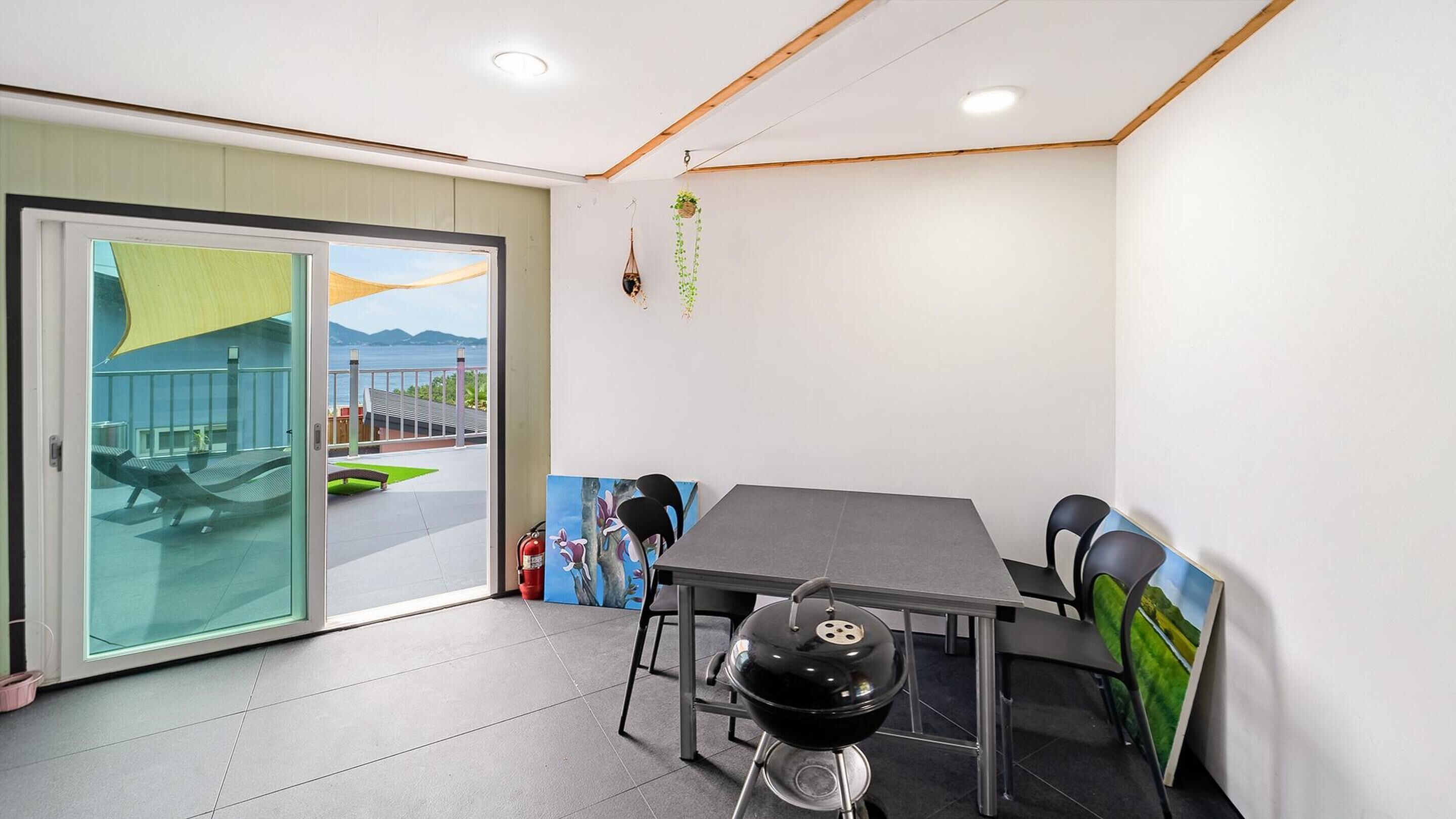 A modern room with a sliding glass door leading to an outdoor area, a black grill, and a table with chairs.