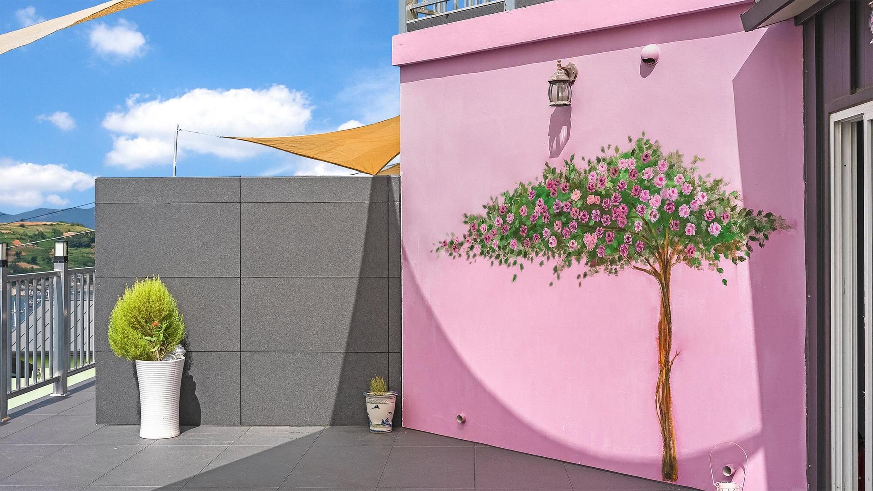 A pink building with a painted tree and a small potted plant.