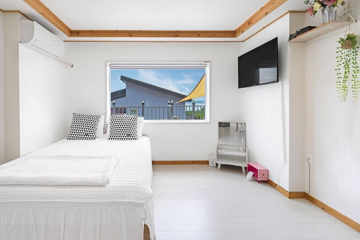 A bedroom with a bed, a window with a view, a TV, and a small table.