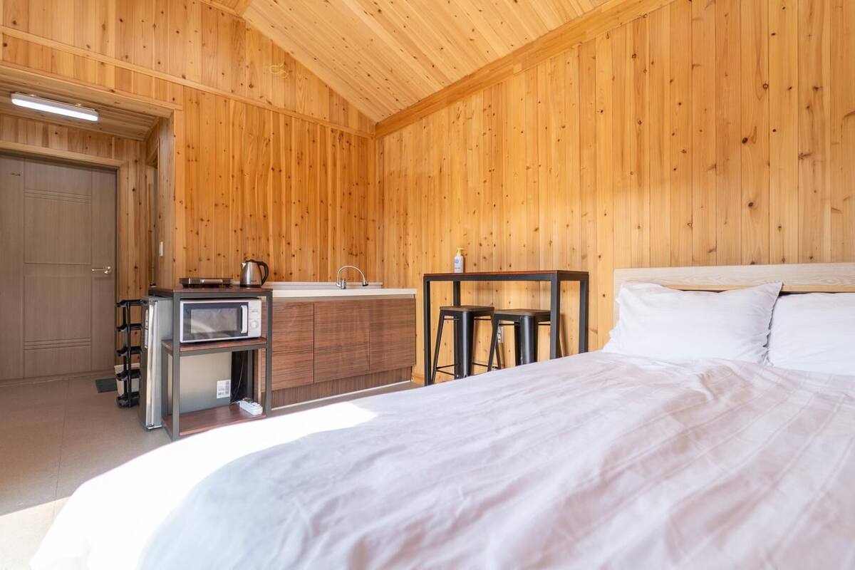 A wooden-paneled room with a bed, a kitchenette, and a door.