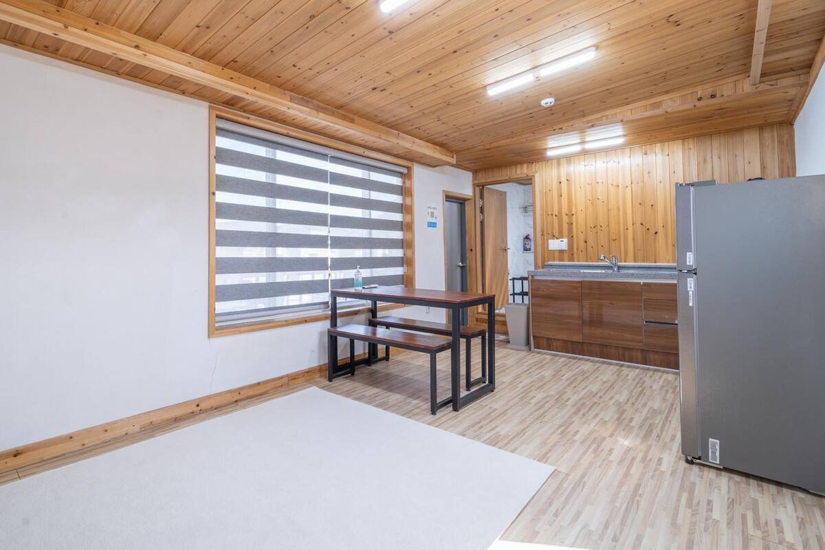 A modern kitchen with wooden cabinets, a stainless steel refrigerator, and a window with blinds.