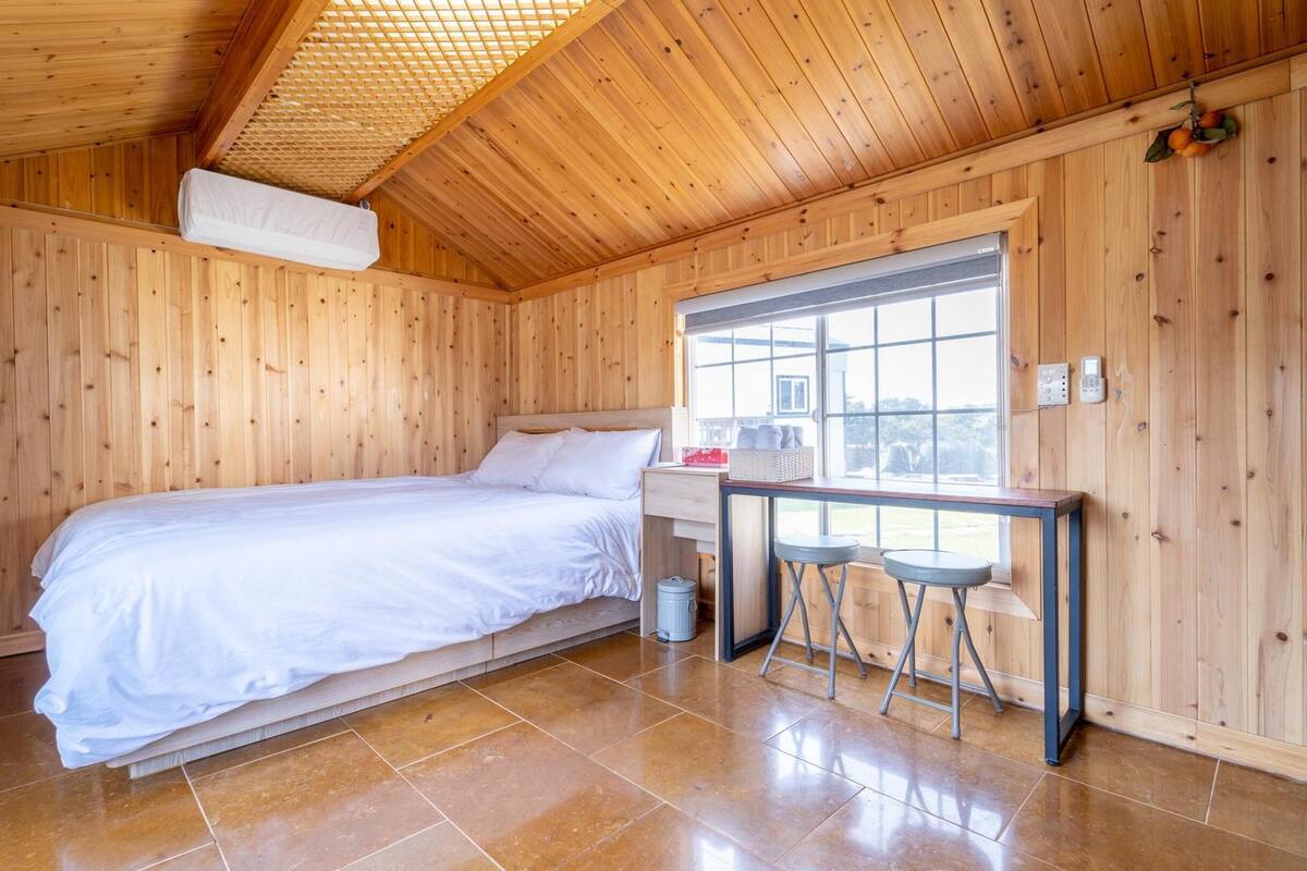 A wooden room with a bed, a window, and a small table with stools.