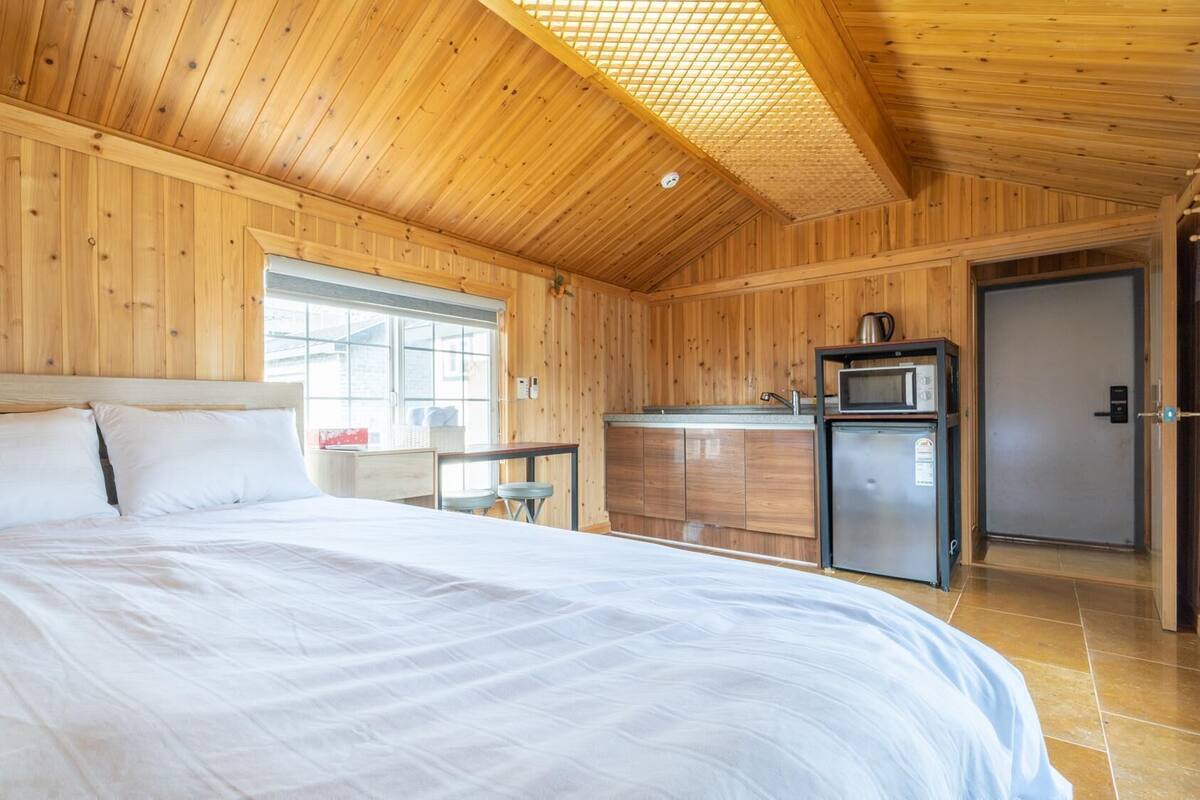 A wooden cabin bedroom with a bed, a small kitchenette, and a door.