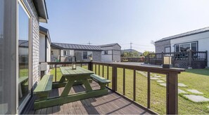 A wooden deck with a picnic table, a fenced yard, and a building with a metal roof. - Jeju Bijalim Pension (Jeju City)