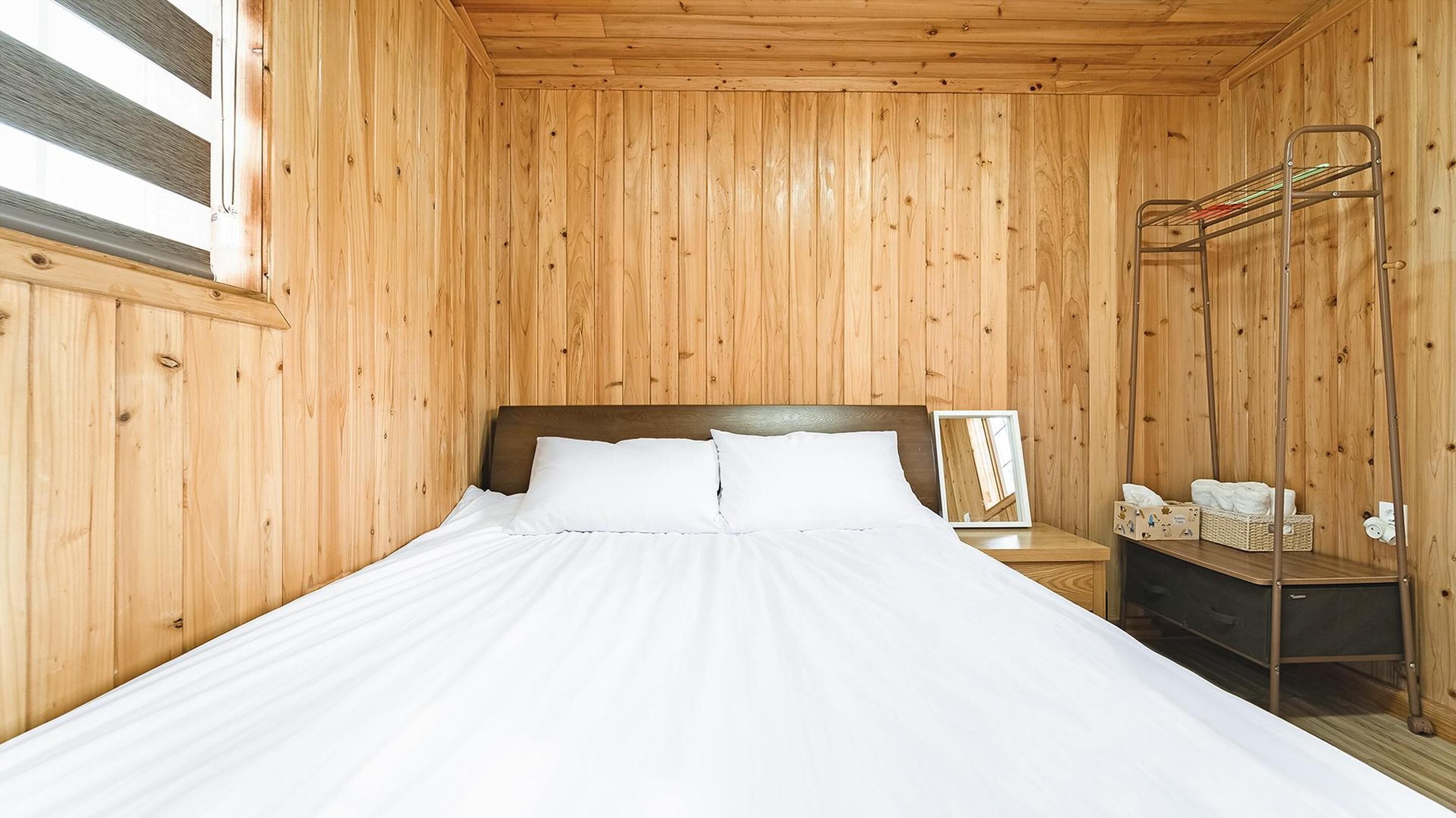 A wooden-paneled room with a bed, a nightstand, and a mirror.