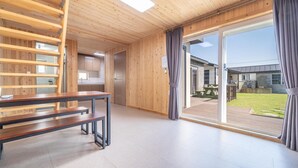A modern interior with a wooden staircase, a dining area with benches, and large sliding glass doors leading to an outdoor deck. - Jeju Bijalim Pension (Jeju City)