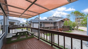 A covered outdoor deck with wooden railings, a picnic table, and a view of neighboring buildings. - Jeju Bijalim Pension (Jeju City)