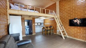 Une pièce de style loft avec un plafond en bois, un lit superposé, un coin cuisine et un téléviseur fixé au mur en briques.