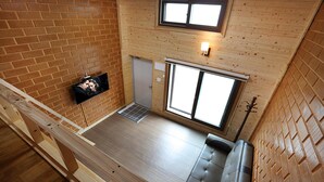 Une pièce de style « loft », avec un plancher en bois, un canapé, un téléviseur fixé au mur et une grande fenêtre laissant entrer la lumière naturelle.