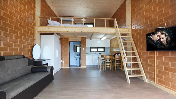 Une chambre de style « loft » avec un lit superposé, un coin cuisine, un espace repas et un téléviseur fixé au mur.