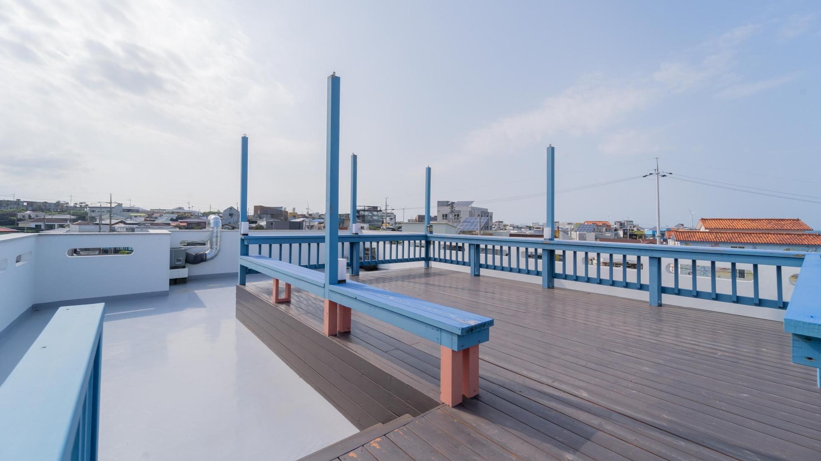 Eine Holzterrasse mit blauen Geländern, einer Bank und Blick auf die Stadtlandschaft im Hintergrund.