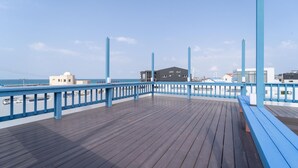 A wooden deck with blue railings overlooking a beach. - Jeju Tunanghouse Pension (Jeju City)