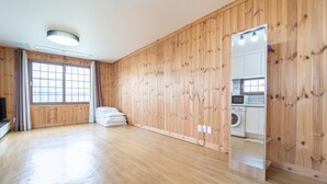 A spacious room with wooden paneling, a large window, a mirror, and a built-in washing machine. - Jeju Tunanghouse Pension (Jeju City)