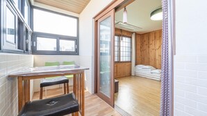 A compact room with a wooden table, two chairs, a bench, and a large window. - Jeju Tunanghouse Pension (Jeju City)