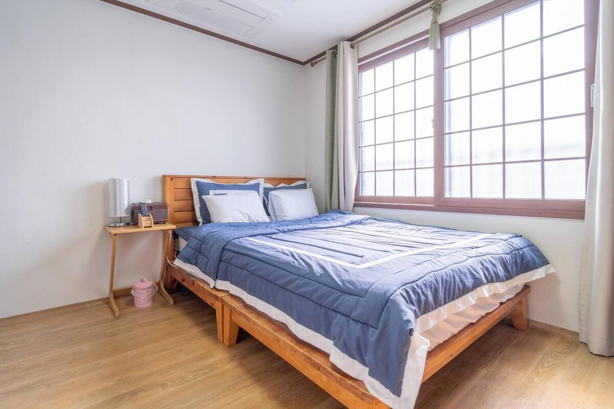 A bedroom with a wooden bed, a bedside table with a lamp, and a window with curtains.
