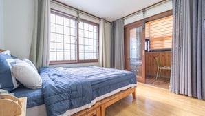 A bedroom with a bed, a wooden bench, a window, and a sliding door leading to a balcony. - Jeju Tunanghouse Pension (Jeju City)
