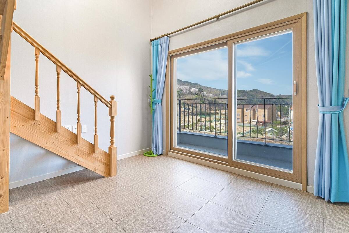 Una habitación con escalera de madera, grandes puertas correderas de vidrio y vista a un área residencial.