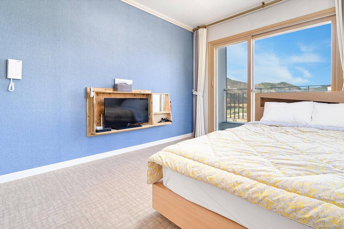 Habitación de hotel con cama, televisor montado y vistas al exterior.