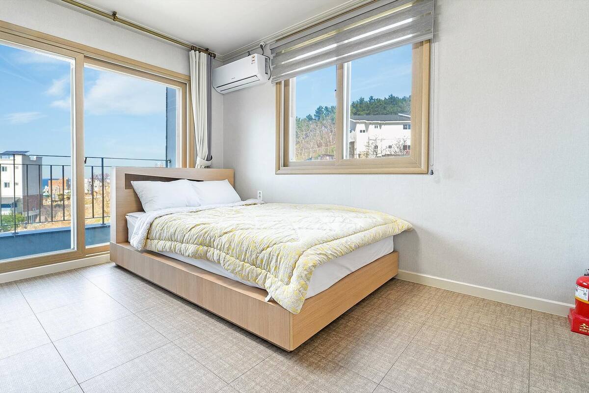 Un dormitorio con cama, ventanas amplias y aire acondicionado.