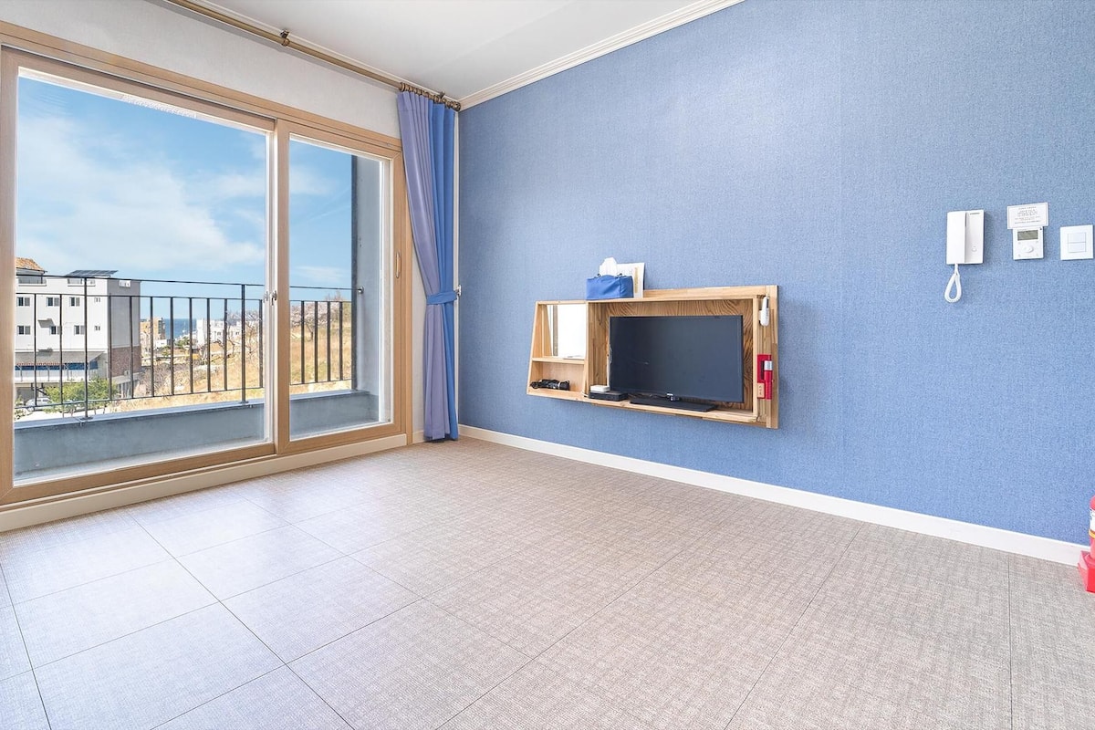 Una habitación con un gran ventanal corredero a un balcón, un televisor de pared y un extintor.