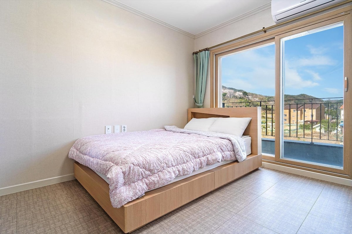 Un dormitorio con cama, ventana con cortinas y vistas al exterior.
