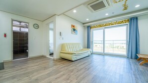 A spacious living area with a sofa, a large window with curtains, and a visible bathroom with a shower. - Jeju Byeoleuldameunbaramarae Pension (Jeju City)