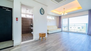 A spacious living room with a sofa, a clock, and a view of the outside.